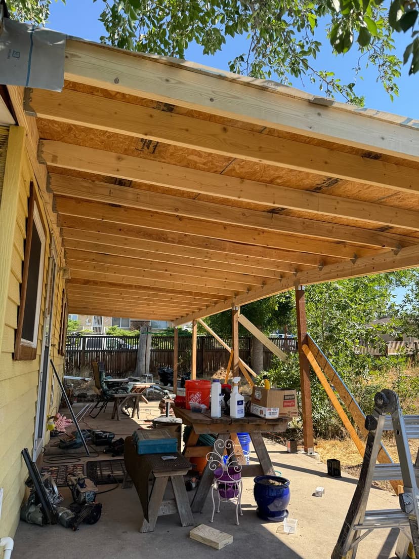 Wooden patio under construction with beams, tools, and patio furniture visible.